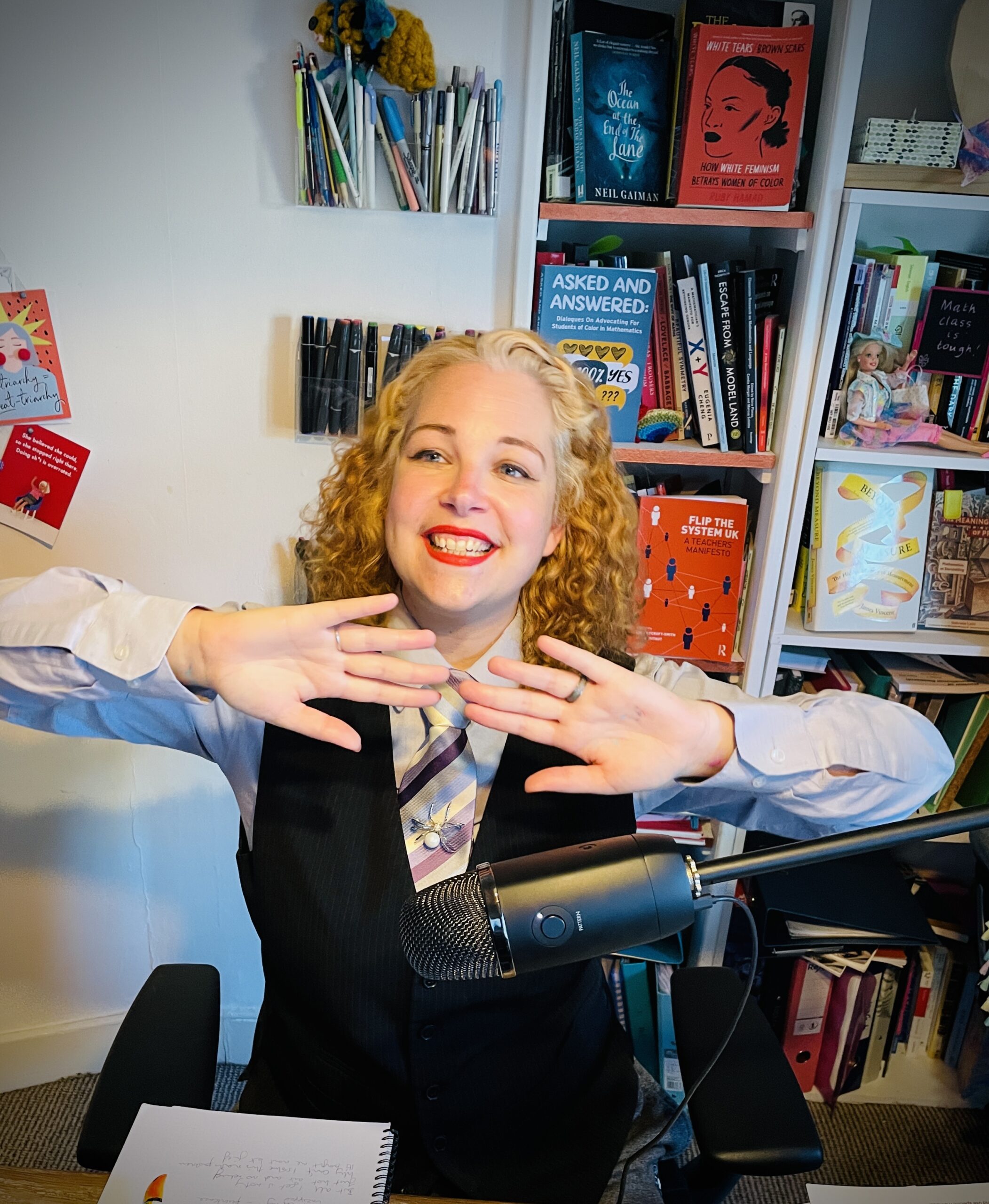 Lucy wearing a long sleeve shirt and multi-colour striped tie smiling with her hands in front of her chest, doing the actions to her song 'Frogs and Slugs'